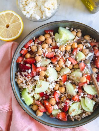 Farro salad with strawberries and cucumbers in a bowl with a spoon.