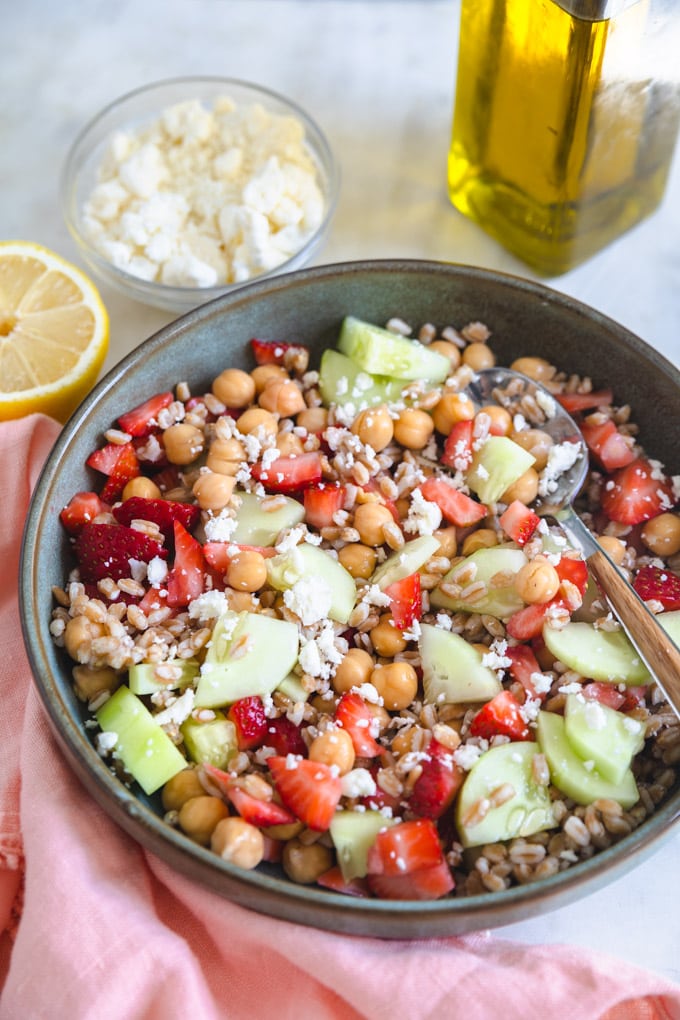 Olive oil, feta and lemon next to a bowl of farro salad. 