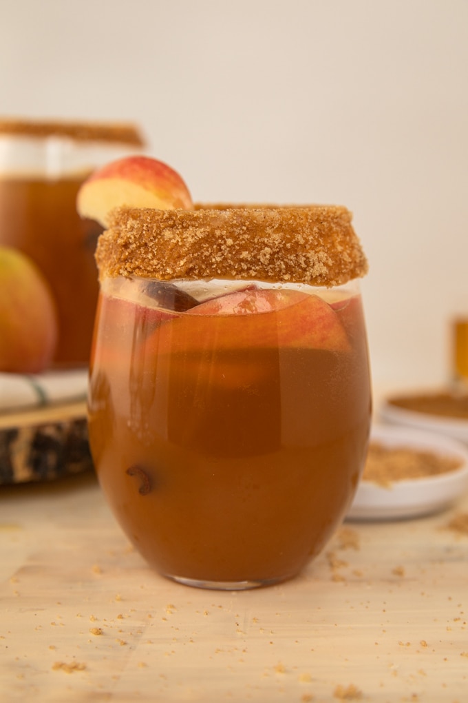 a glass full of apple cider, apples and a cinnamon stick. 