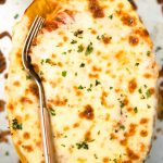 a squash on a baking sheet with a fork and cheese on top.