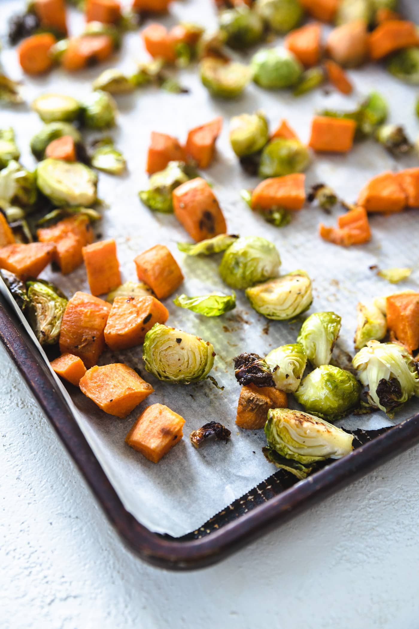 A baking sheet lined with parchment paper with sweet potatoes and brussel sprouts on it.