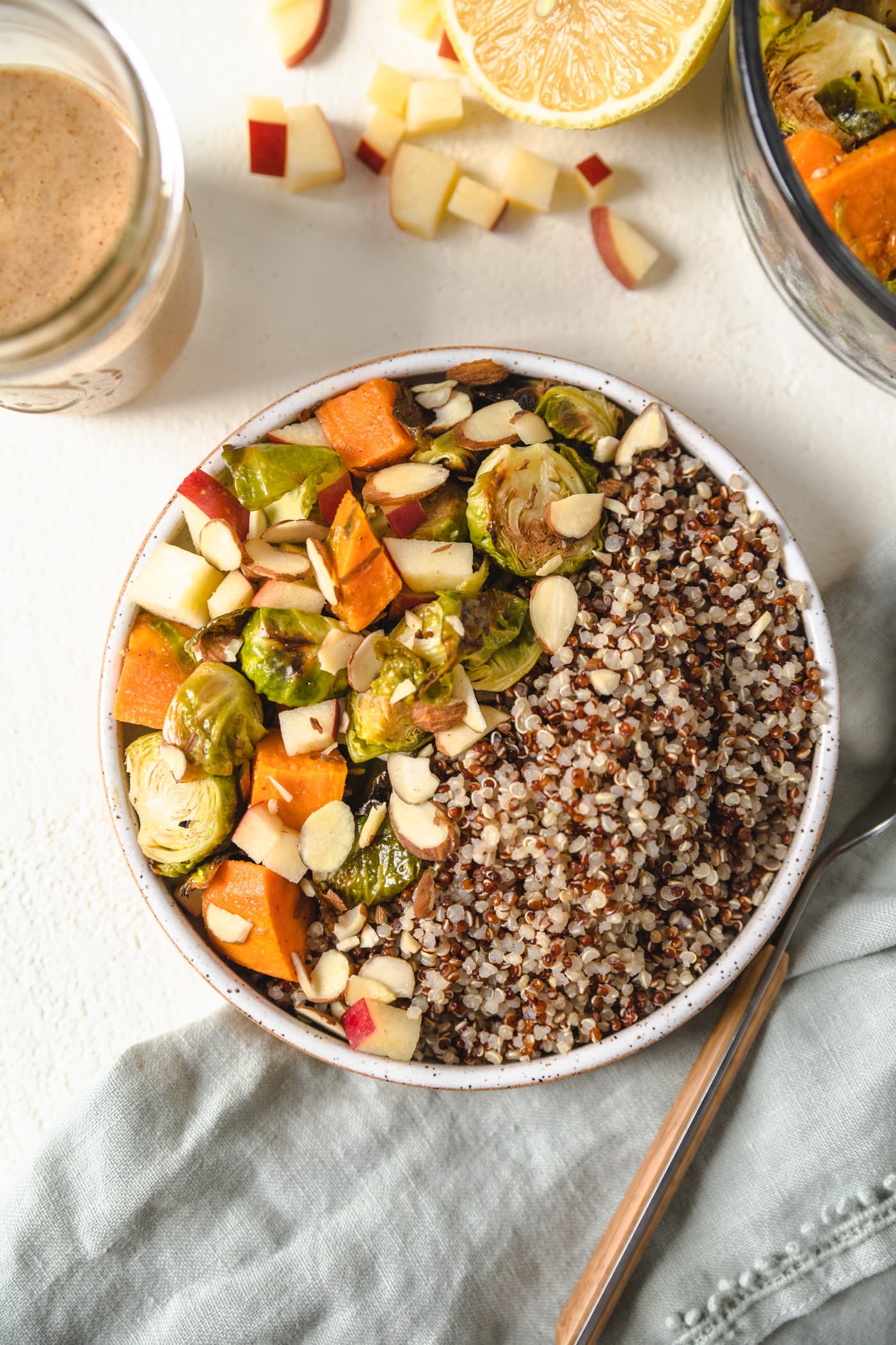 A buddha bowl filled with fall vegetables, quinoa next to a jar of almond ginger dressing.