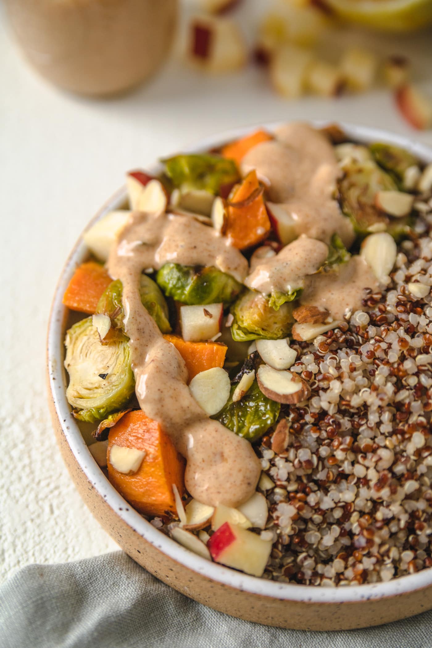 A buddha bowl filled with vegetables and quinoa and drizzled with almond ginger dressing. 