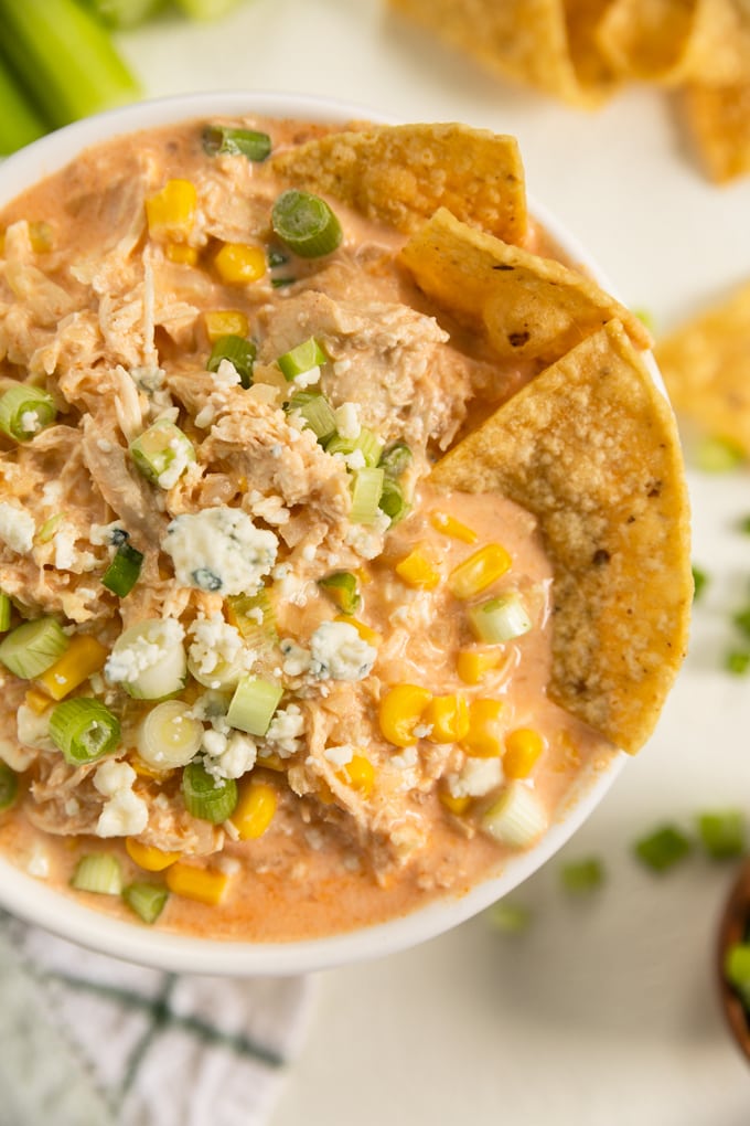 a bowl of buffalo chicken dip with tortillas being dunked into it. 