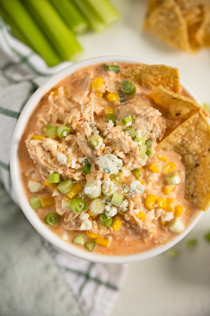 blue cheese, corn and tortilla chips in a bowl of buffalo chicken dip. 