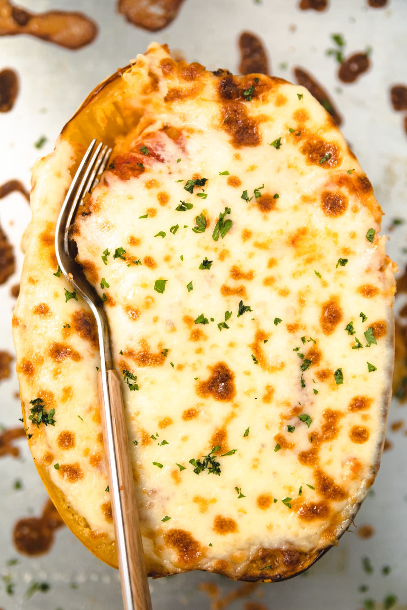 A fork inserted into cheese on top of a spaghetti squash.