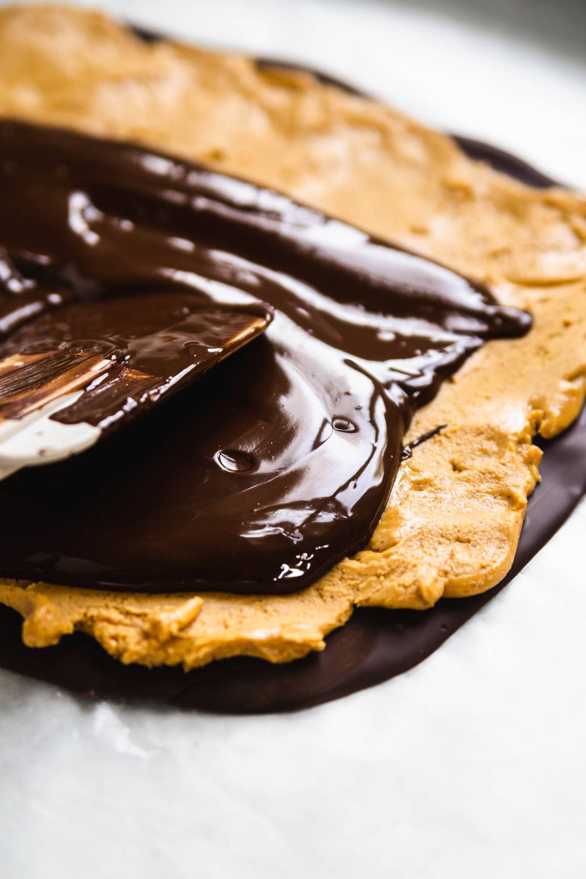 chocolate being poured over top of the peanut butter layer in this peanut butter chocolate bark recipe.