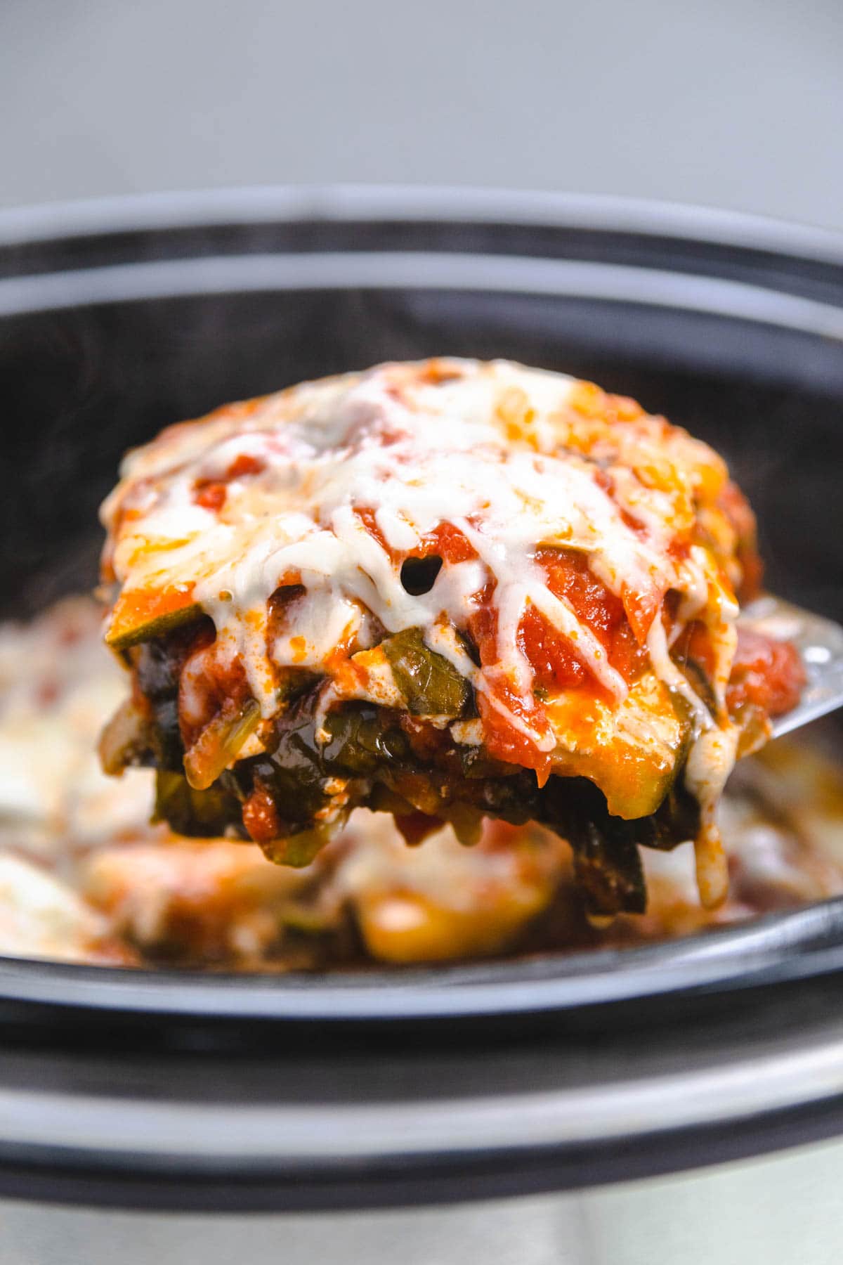 a slice of vegetarian noodle less lasagna on a spatula being lifted from a crockpot.