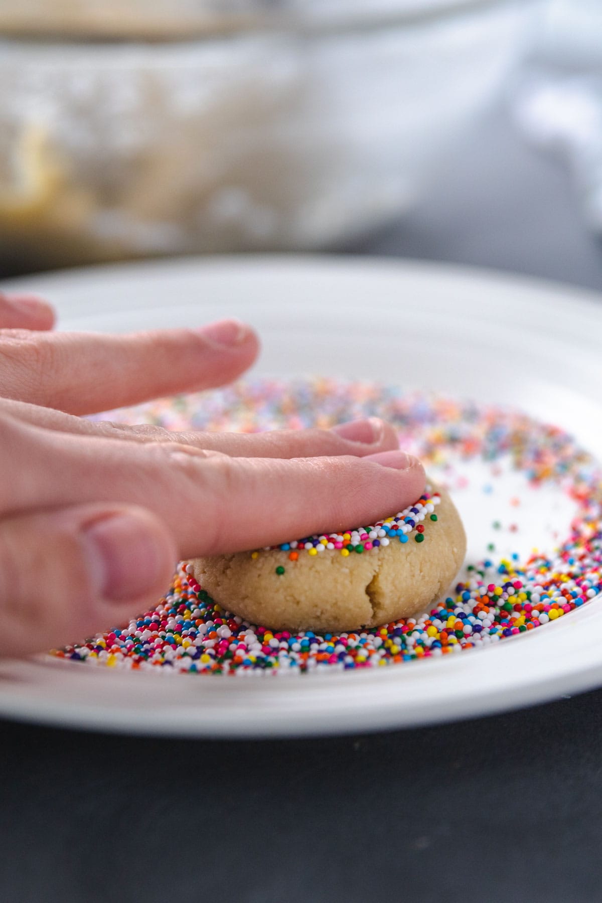 Fingers gently pressing down on cookie with sprinkles. 