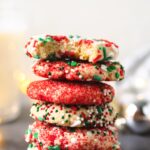 a stack of holiday sprinkle cookies with a bite taken out of the top one.