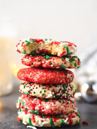 a stack of holiday sprinkle cookies with a bite taken out of the top one.