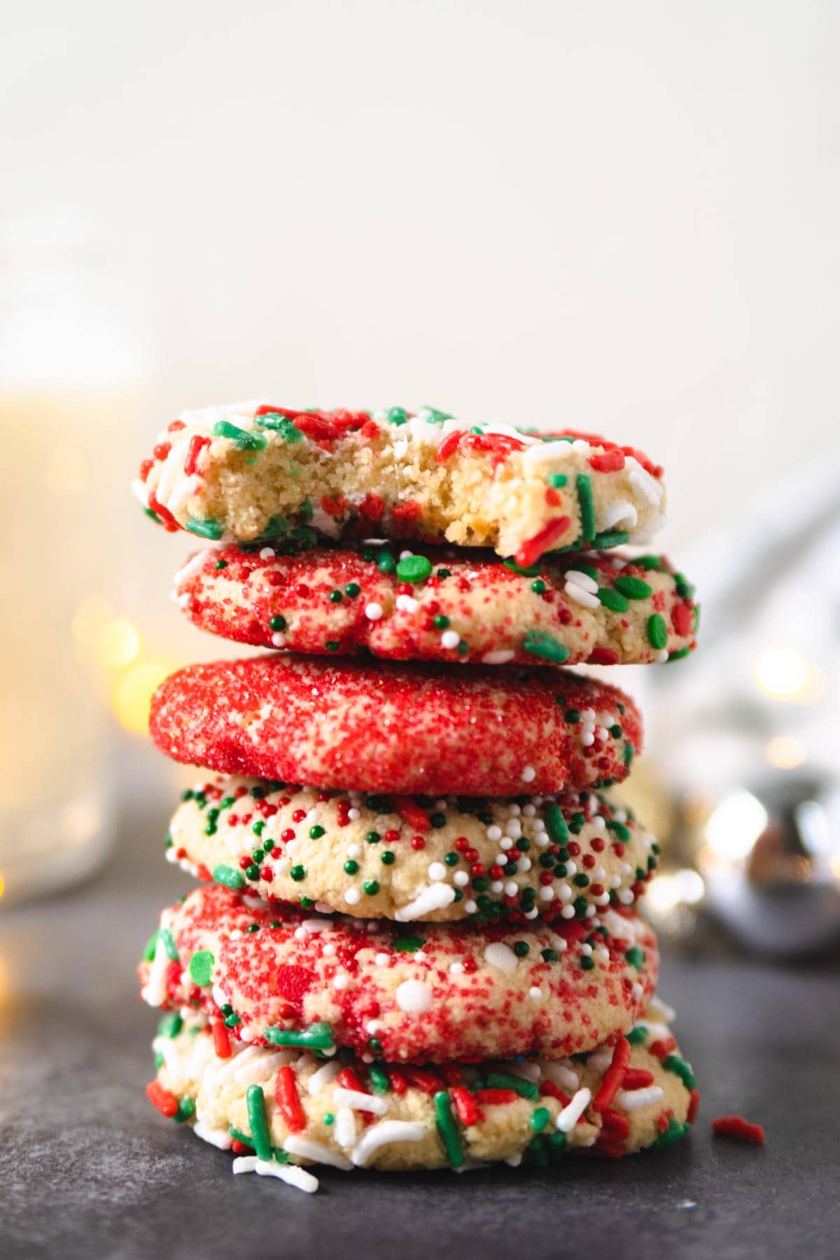 sprinkle cookies stacked on top of one another with Christmas lights in the background.