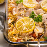 a casserole dish with a spoon serving lemon and chicken.