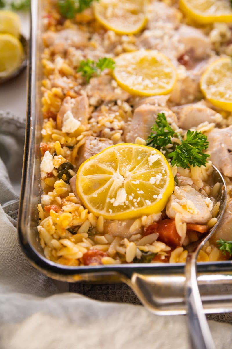 a casserole dish with a spoon serving lemon and chicken.