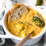 chicken broccoli cheddar soup in a bowl with a spoon and a slice of bread.