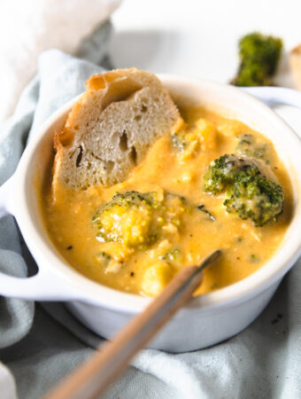 chicken broccoli cheddar soup in a bowl with a spoon and a slice of bread.