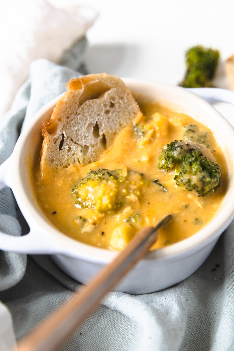 a bowl of broccoli cheddar soup with chicken and a piece of sourdough sticking out of the top of the bowl.