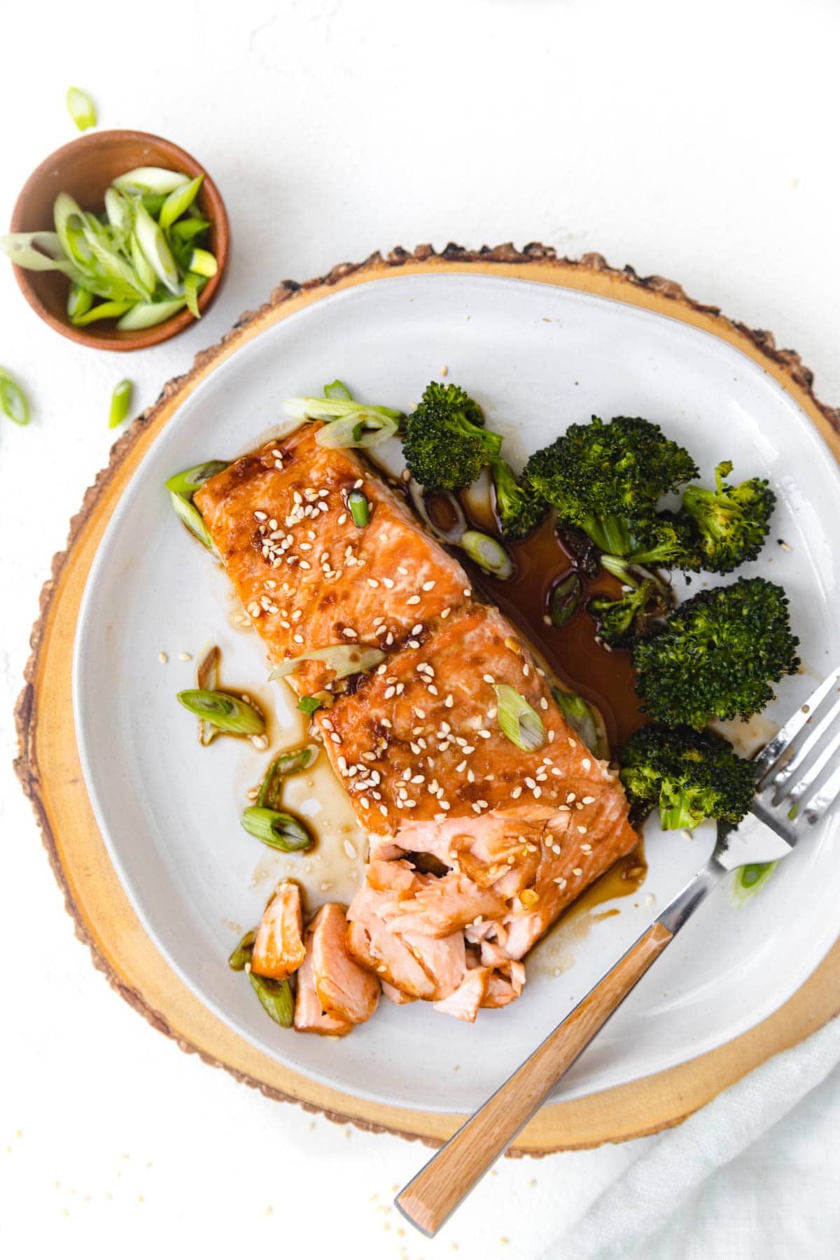 salmon on a plate with broccoli and fork. Sauce dripping off the salmon onto the plate. 