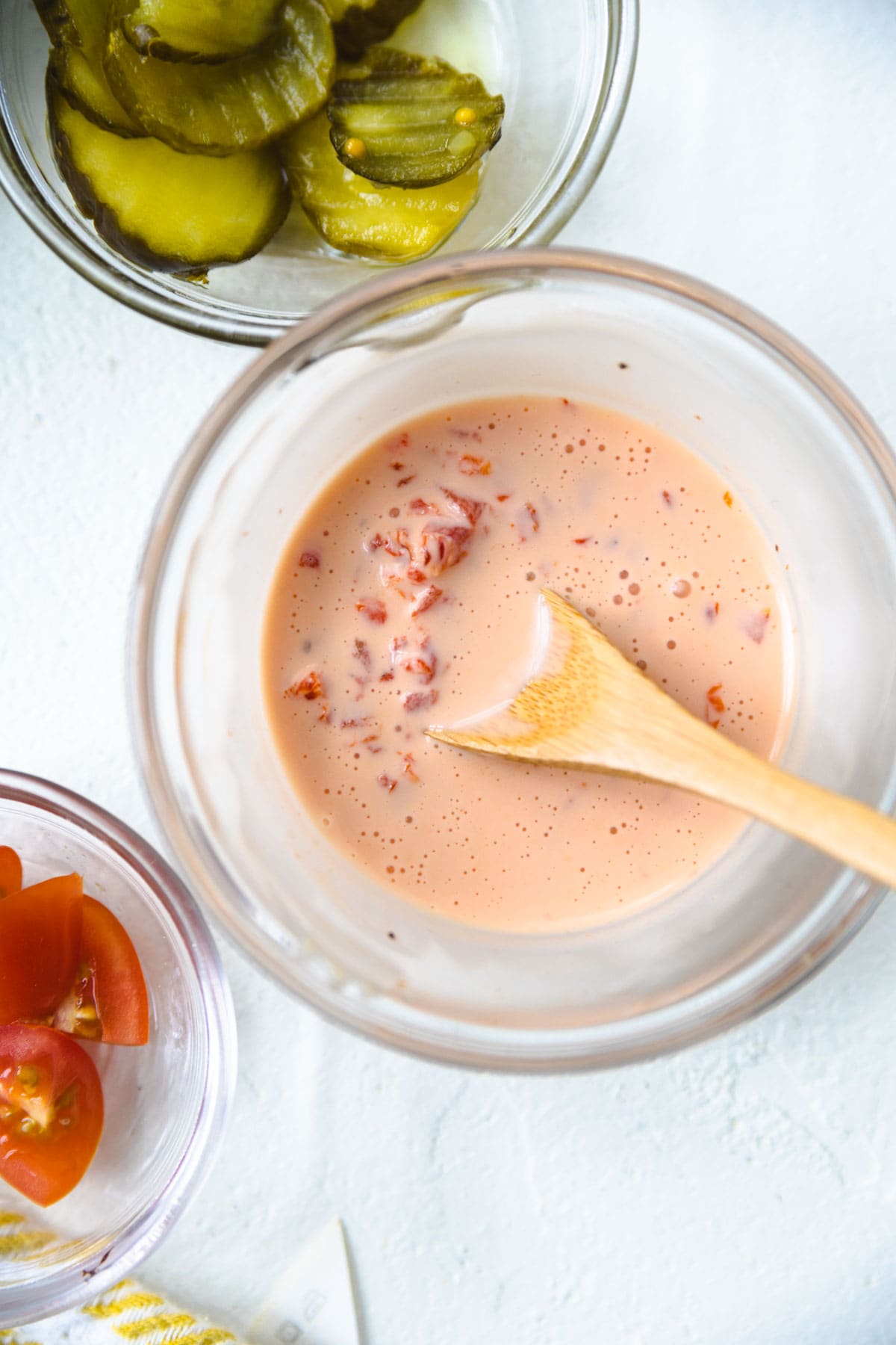 AIOLI IN A SMALL BOWL MIXED WITH RED ROASTED PEPPERS WITH A WOODEN SPOON.