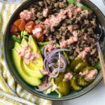 A BOWL FILLED WITH BURGER BOWL INGREDIENTS WITH AIOLI SAUCE ON TOP AND A FORK.