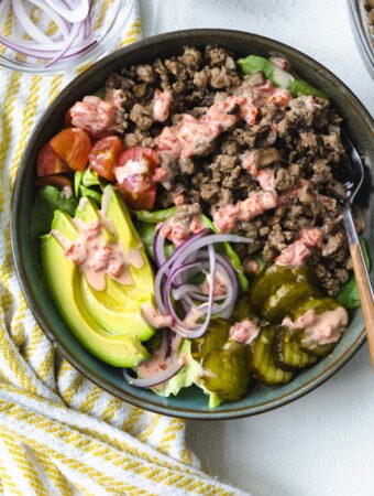 A BOWL FILLED WITH BURGER BOWL INGREDIENTS WITH AIOLI SAUCE ON TOP AND A FORK.