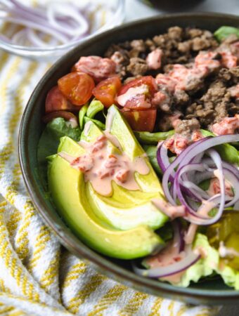 AVOCADO AND BURGER TOPPINGS IN A BOWL WITH AIOLI ON TOP.
