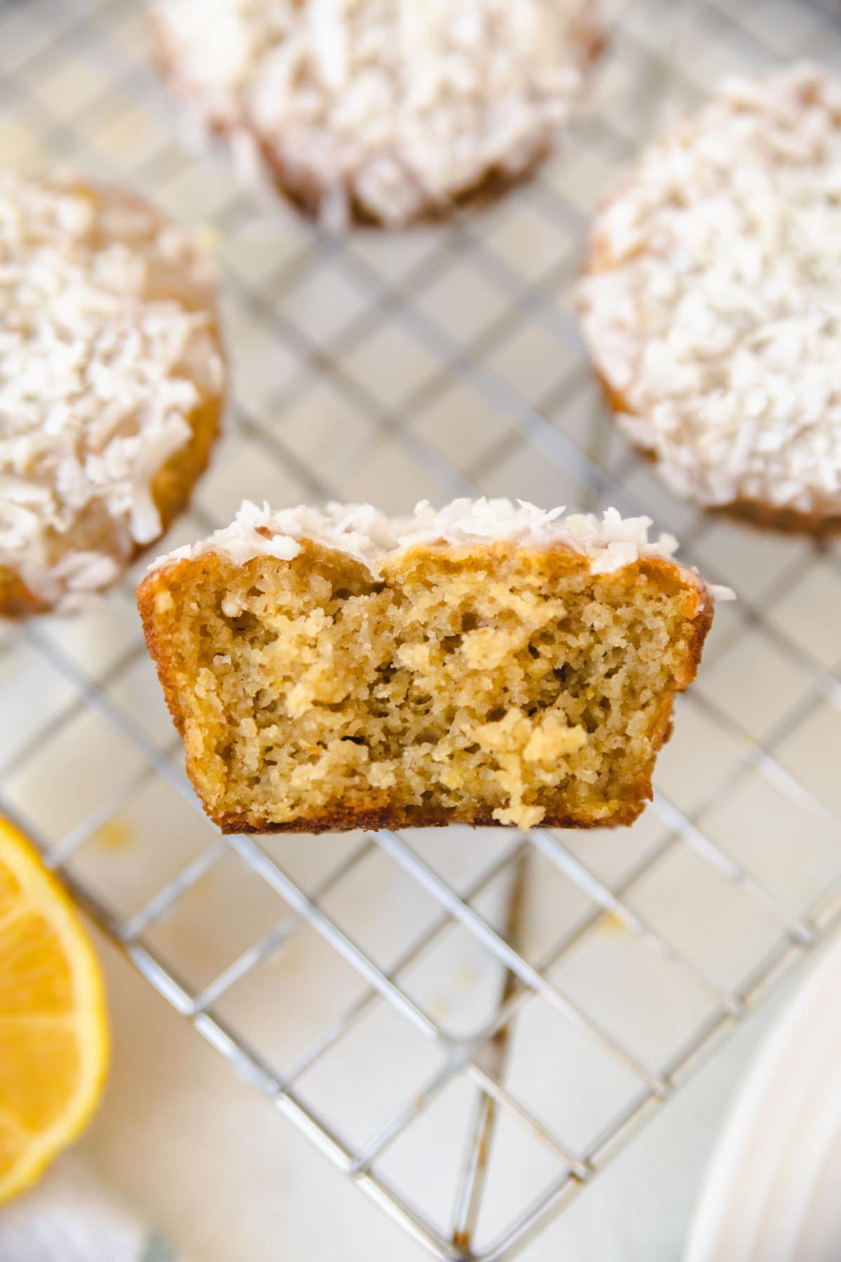 The inside of a lemon coconut muffin next to other muffins on a cooling rack. Shredded coconut on top. 