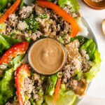 a plate of lettuce wraps with a bowl of peanut sauce in the middle.