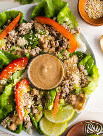 a plate of lettuce wraps with a bowl of peanut sauce in the middle.