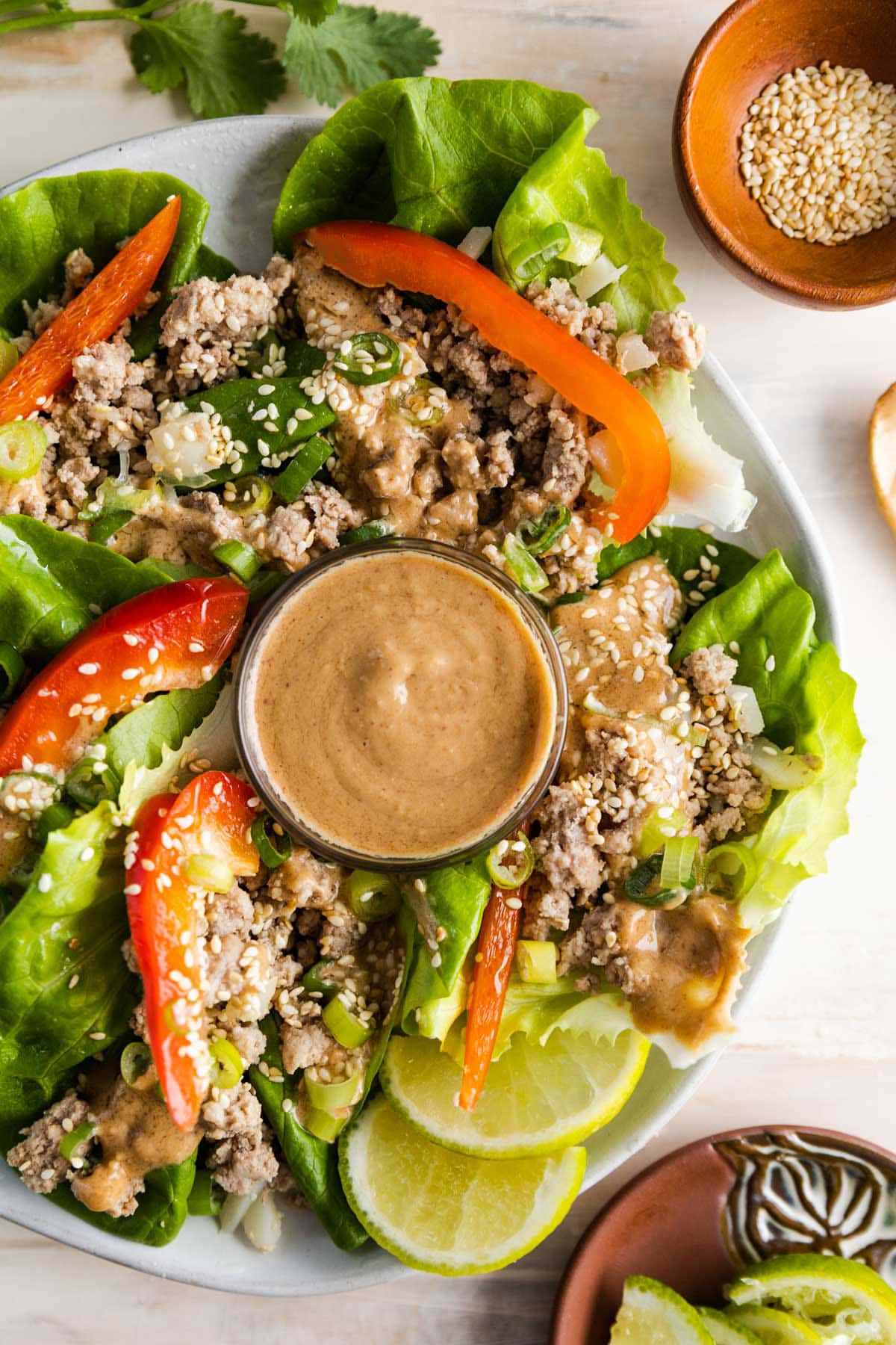 lettuce wraps on a plate filled with ground turkey, peanut sauce and topped with sesame seeds, bell peppers and onions.