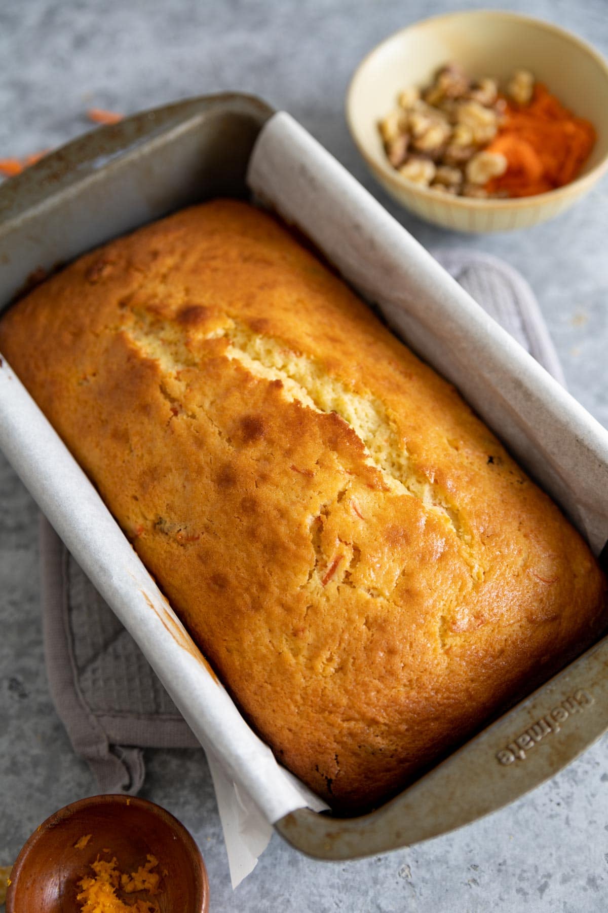 the carrot cake bread in a loaf pan, unfrosted with orange zest and walnuts next to it.