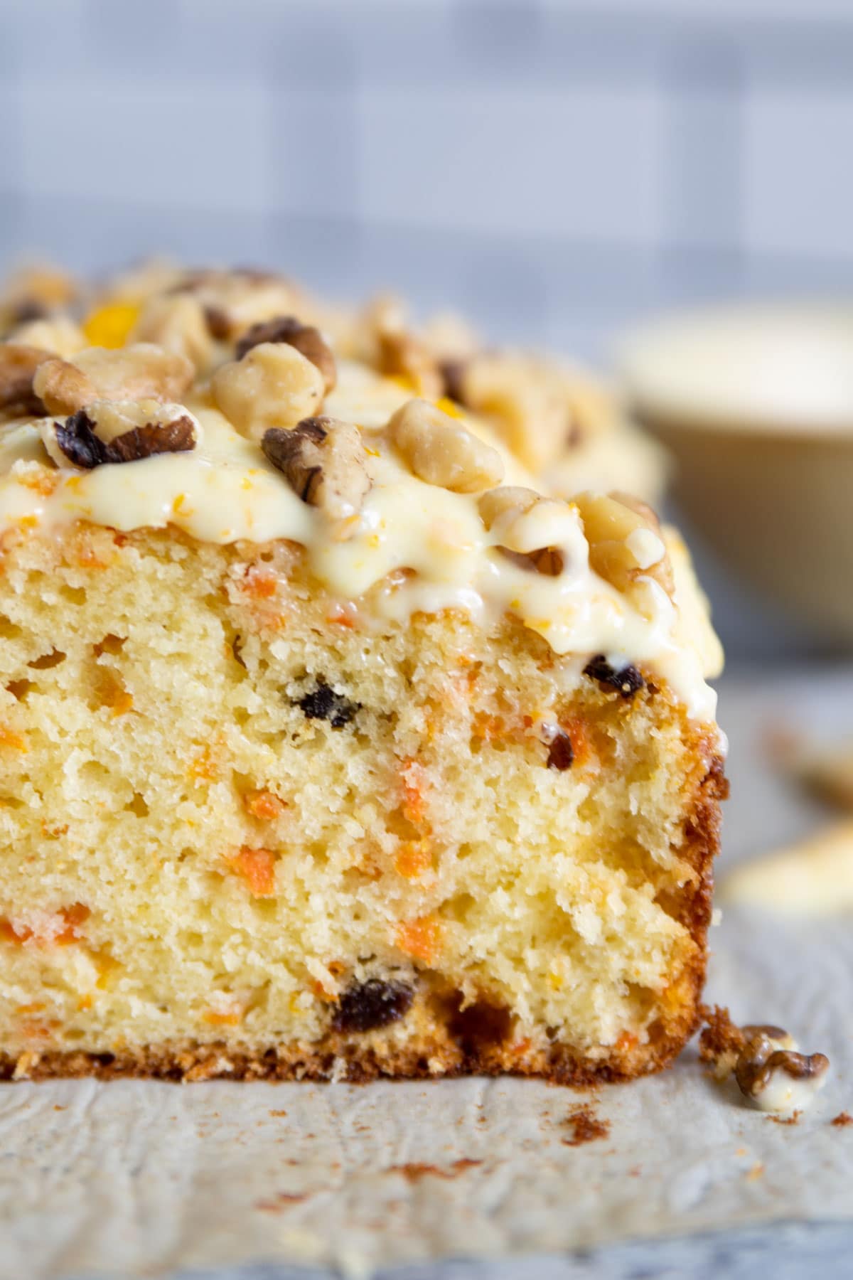 up close shot of frosting on the bread with walnuts on top. Carrot and raisins are inside the bread.