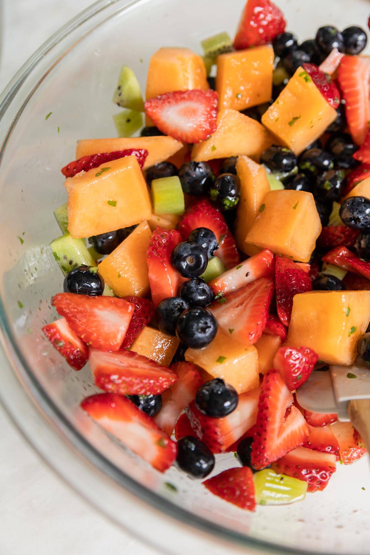 A bowl of fruit salad tossed in a honey basil dressing and served with a spoon.