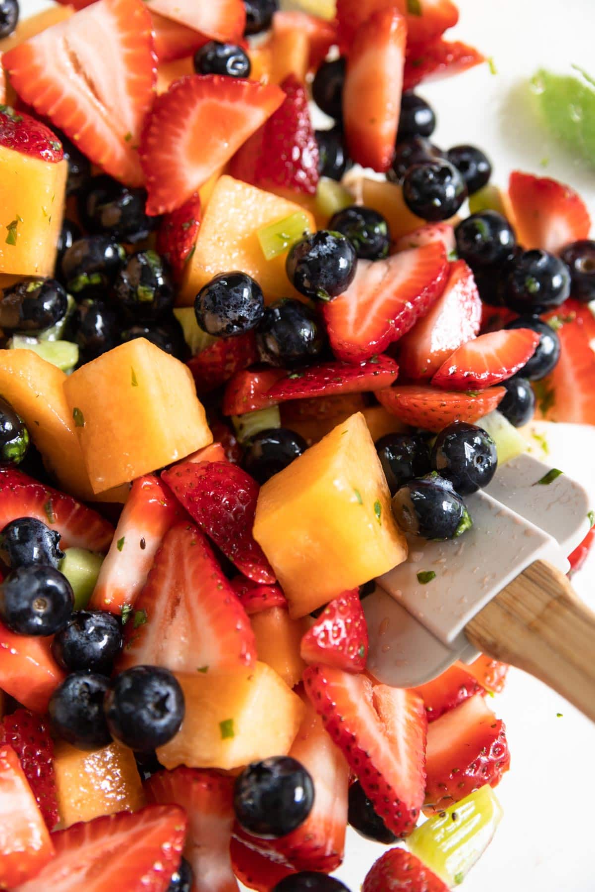 Strawberries, blueberries, melon and kiwi in a bowl with basil lemon dressing on top.